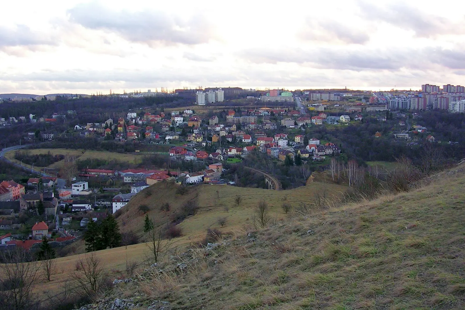 A view over the roofs of Hlubočepy in south-west Prague from a grassy hillside, with housing estates on the horizon