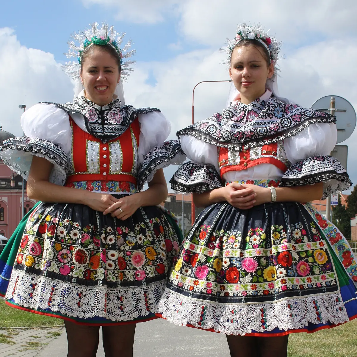 Two young women in festive Slovácko costume with full skirts embroidered in bright flowers, white puffed sleeves and tall black boots