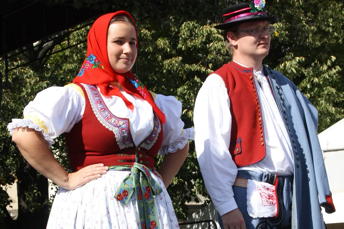 A young couple in Slovácko costume: the woman in a white blouse, red vest and embroidered apron with a red headscarf, the man in a white shirt, red vest and blue trousers