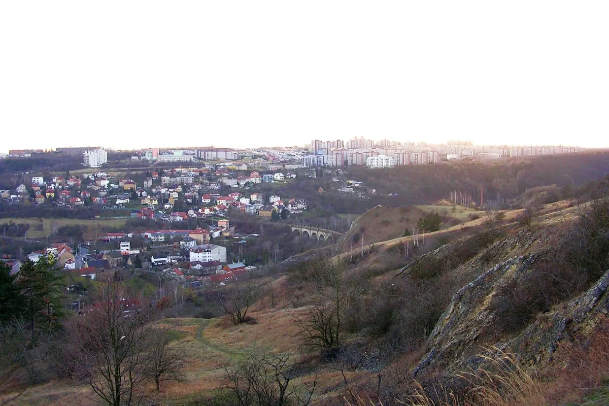 A view over the roofs of Hlubočepy in south-west Prague from a grassy hillside, with a viaduct and housing estates beyond